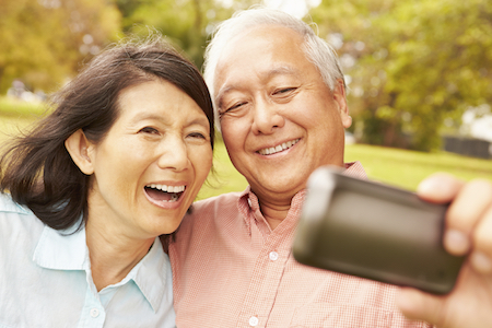 Happy Asian couple smiling for a selfie knowing the dental implants make their smiles look natural and perfect. 